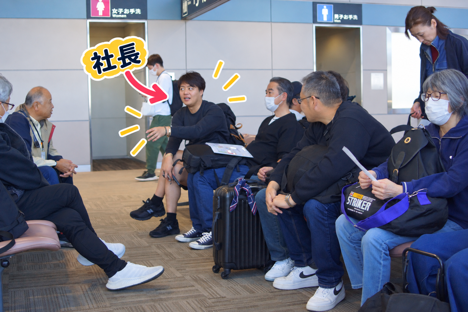 出発前の空港。上着姿の社員たちの中で半ズボン姿の社長